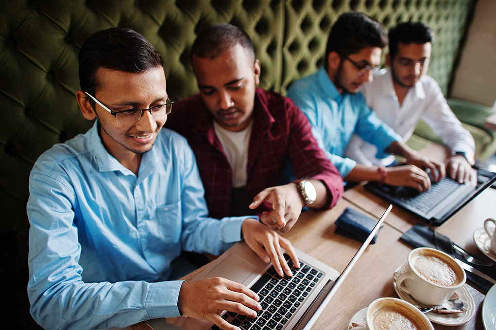 Diverse young men looking at computer screens in conversation